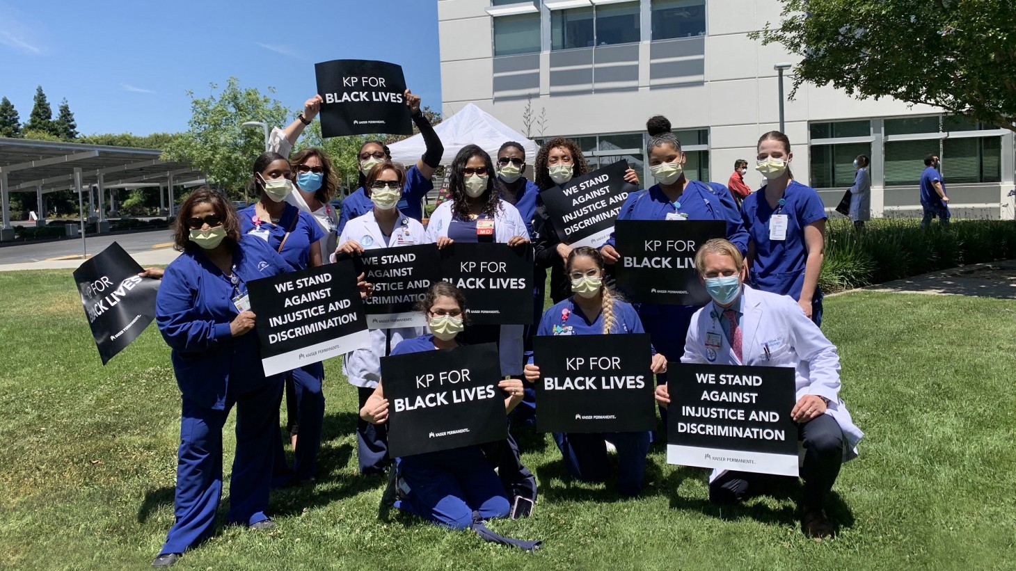 一群身穿手术服、戴着口罩的医护人员，举着写有“为黑人的生命而KP”的标语。