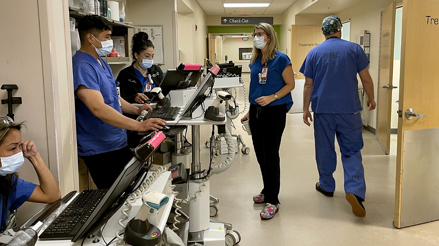 4 health care workers wearing blue scrubs in a busy emergency room hallway