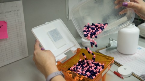 a pair of hands pouring black and pink pills into a box