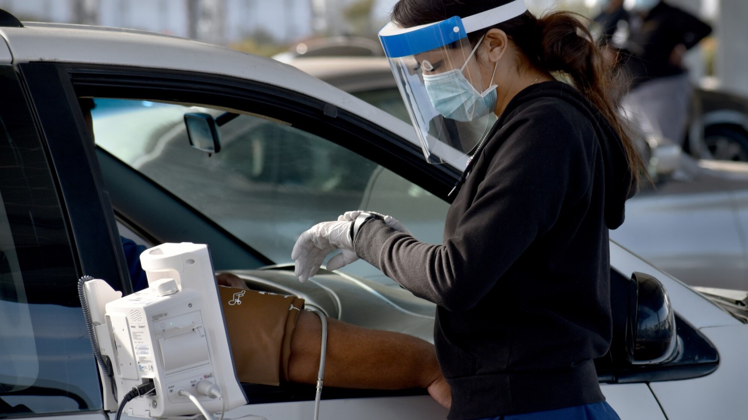 女人戴着面罩检查一个人的血压在他坐在车座上的一辆汽车
