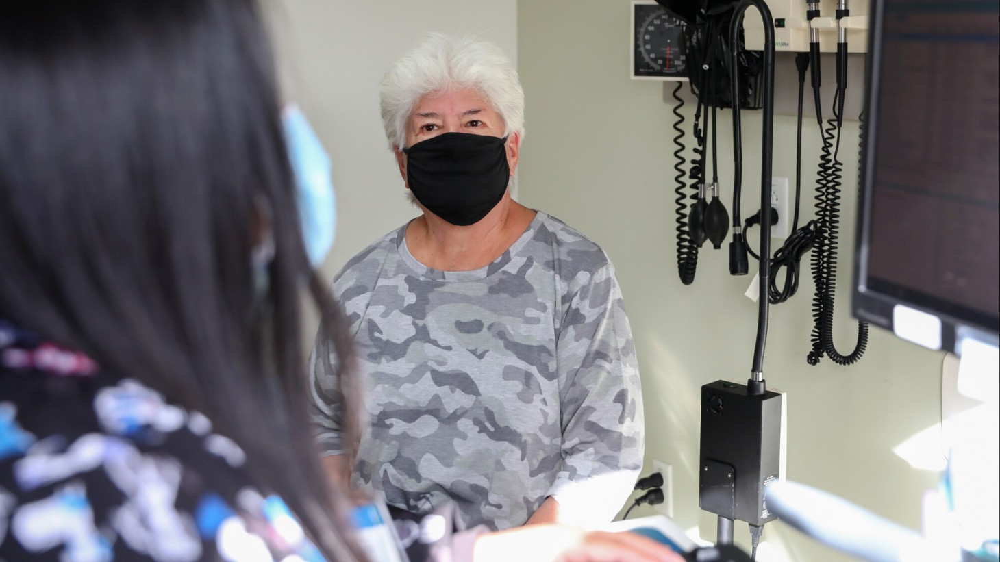 年长的女病人在医生办公室，戴着口罩